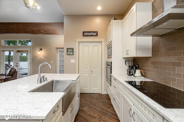 kitchen featuring dark wood-type flooring, wall chimney exhaust hood, light stone counters, appliances with stainless steel finishes, and white cabinets