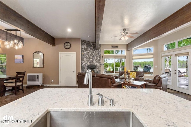 kitchen with sink, hanging light fixtures, light stone counters, a stone fireplace, and beamed ceiling