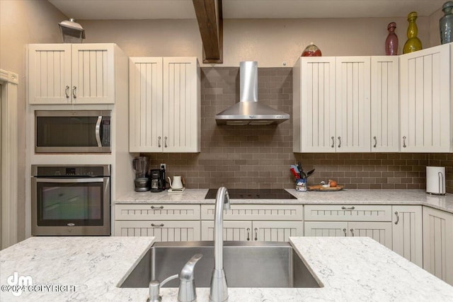 kitchen with sink, light stone counters, stainless steel appliances, decorative backsplash, and wall chimney range hood