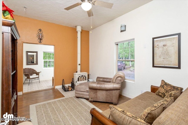 living room with hardwood / wood-style flooring, ceiling fan, a textured ceiling, and a wood stove