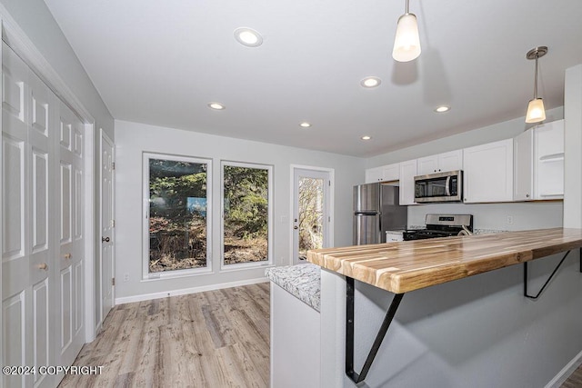 kitchen featuring kitchen peninsula, hanging light fixtures, wooden counters, white cabinets, and appliances with stainless steel finishes