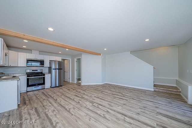 kitchen featuring light hardwood / wood-style flooring, white cabinetry, appliances with stainless steel finishes, beamed ceiling, and sink