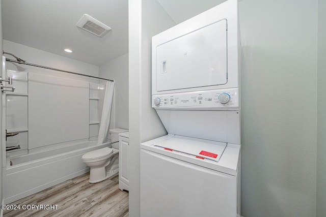 bathroom with toilet, wood-type flooring, shower / bathtub combination with curtain, and stacked washer / dryer