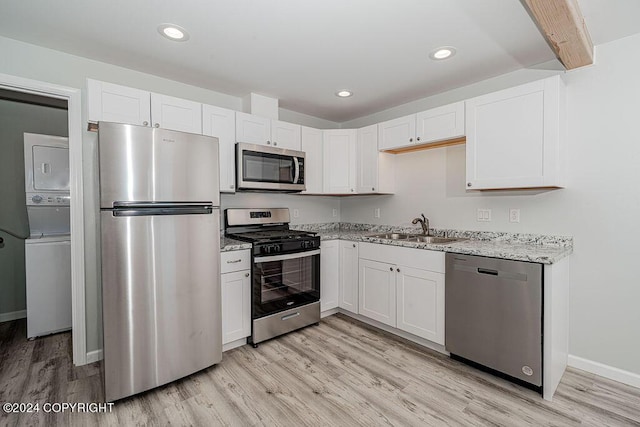 kitchen featuring sink, stainless steel appliances, stacked washer / dryer, and white cabinets