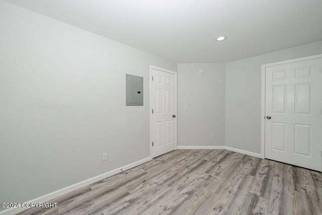 spare room featuring electric panel and light hardwood / wood-style floors