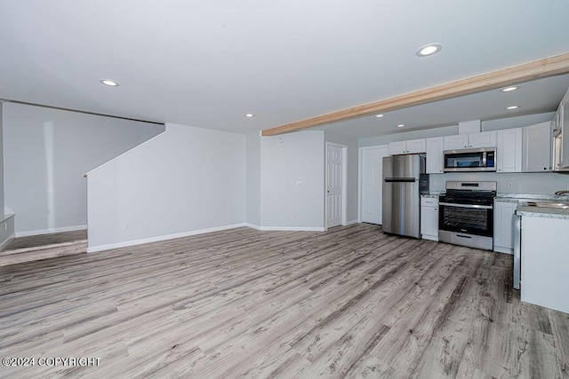 kitchen featuring stainless steel appliances, light wood-type flooring, white cabinetry, beamed ceiling, and sink