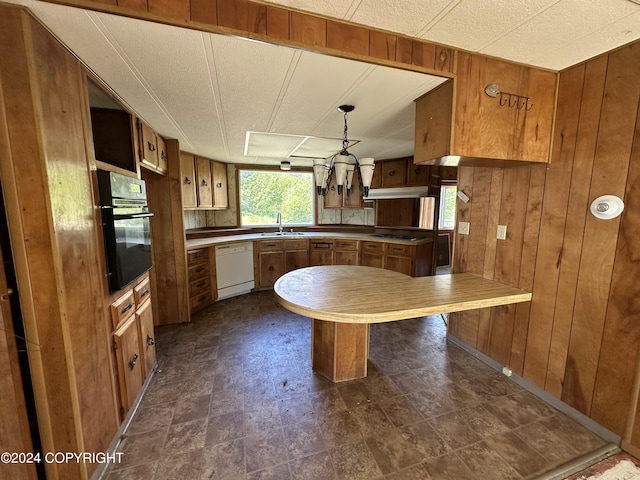 kitchen with dishwasher, hanging light fixtures, black oven, wooden walls, and sink