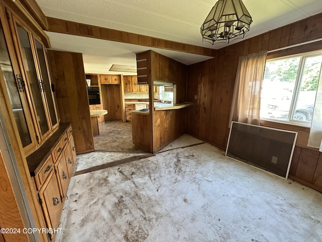 kitchen featuring kitchen peninsula, hanging light fixtures, wood walls, oven, and an inviting chandelier