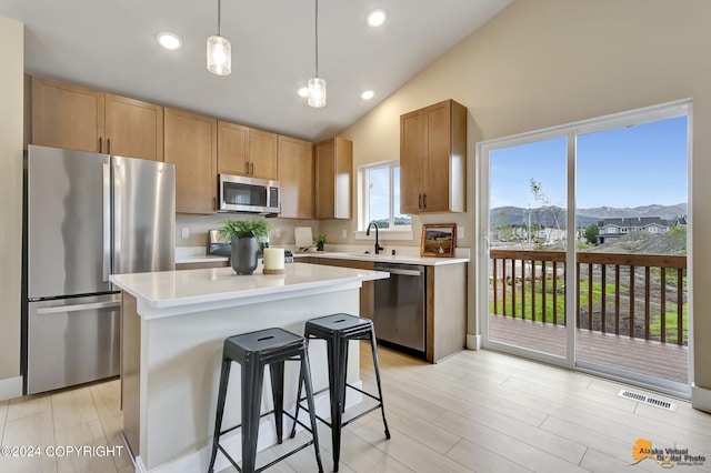 kitchen with stainless steel appliances, a center island, hanging light fixtures, vaulted ceiling, and a breakfast bar area