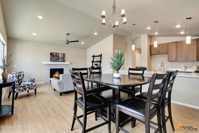 dining area featuring lofted ceiling, a tile fireplace, ceiling fan with notable chandelier, and light hardwood / wood-style flooring