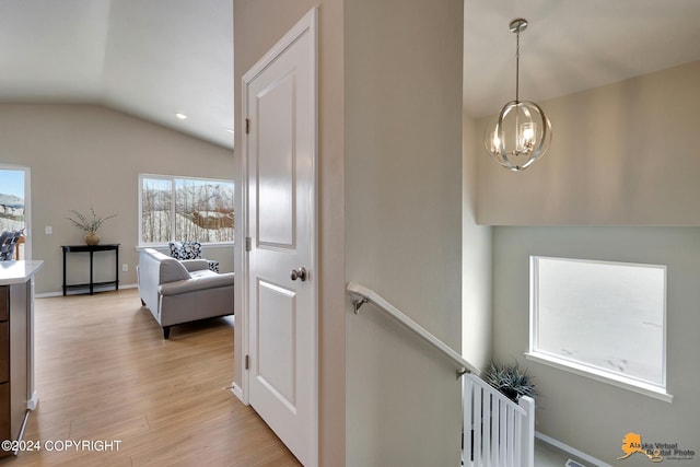 hallway featuring light wood-type flooring, lofted ceiling, plenty of natural light, and a notable chandelier