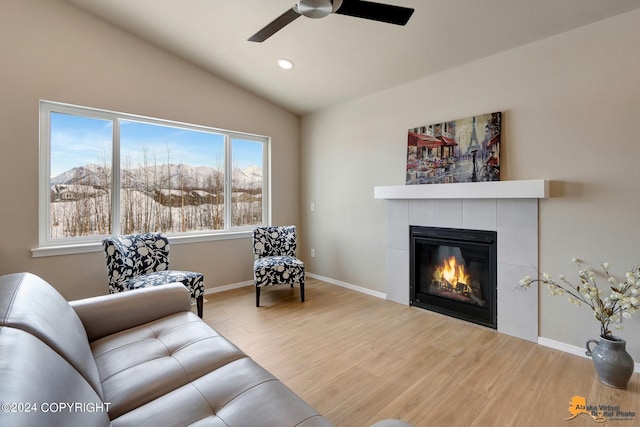 living room with hardwood / wood-style flooring, ceiling fan, a tiled fireplace, and vaulted ceiling