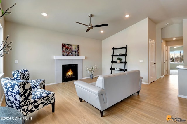 living room with ceiling fan, vaulted ceiling, a fireplace, and light hardwood / wood-style flooring