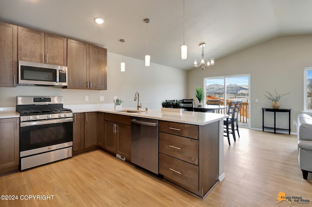 kitchen with kitchen peninsula, stainless steel appliances, hanging light fixtures, vaulted ceiling, and light hardwood / wood-style flooring