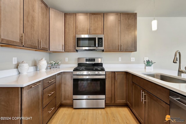 kitchen with light hardwood / wood-style floors, sink, pendant lighting, and stainless steel appliances