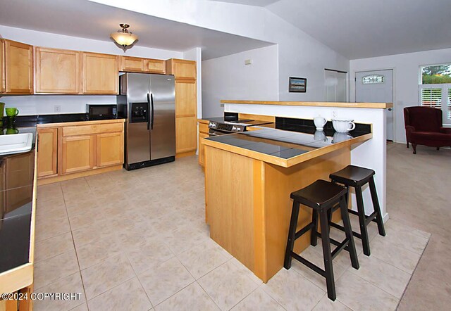 kitchen featuring tile countertops, lofted ceiling, light tile patterned flooring, appliances with stainless steel finishes, and a kitchen breakfast bar