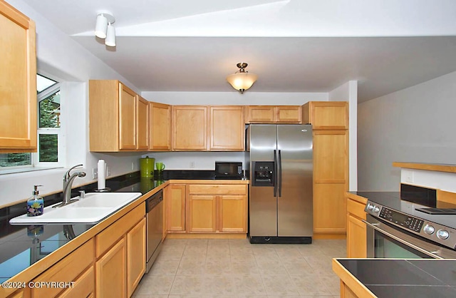 kitchen featuring light tile patterned flooring, a sink, light brown cabinetry, stainless steel appliances, and dark countertops