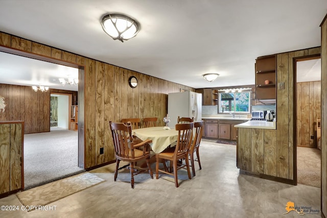 carpeted dining area with wood walls and a chandelier