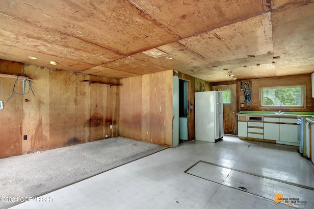 interior space with white fridge, wooden walls, dishwashing machine, and light tile patterned floors