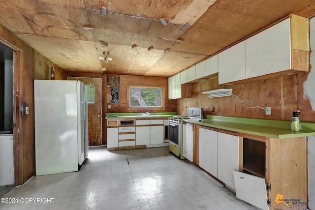 kitchen featuring wooden walls, sink, white cabinets, white fridge, and stainless steel range