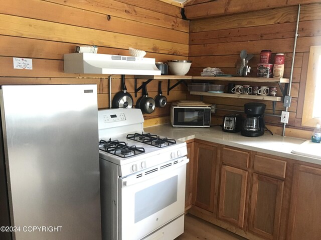 kitchen featuring stainless steel fridge, white gas range oven, wooden walls, and light hardwood / wood-style floors