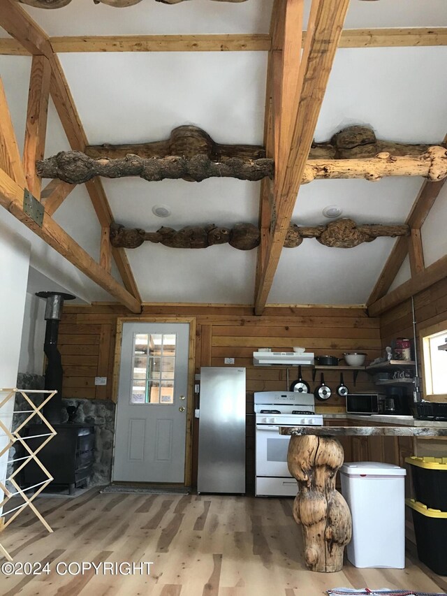 kitchen featuring hardwood / wood-style flooring, a wood stove, lofted ceiling with beams, white range, and stainless steel refrigerator