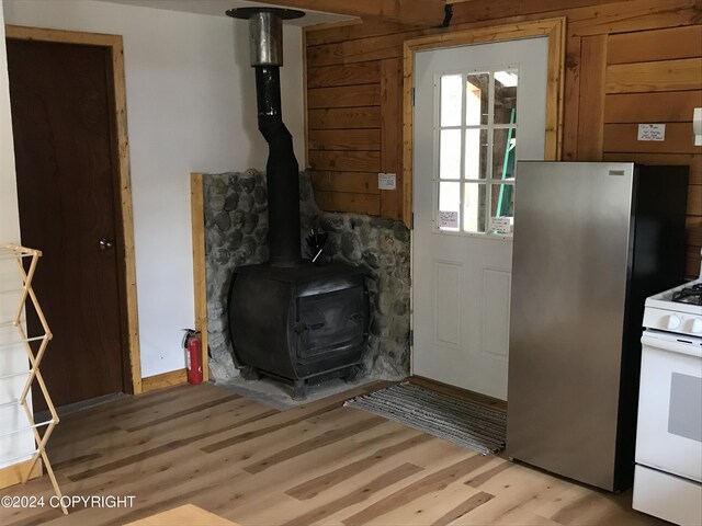 interior space featuring stainless steel fridge, a wood stove, white range with gas cooktop, light wood-type flooring, and wood walls