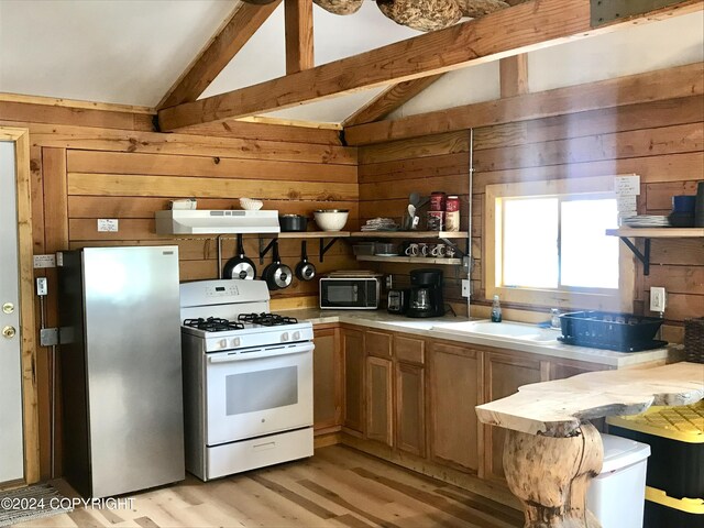 kitchen featuring light hardwood / wood-style flooring, wooden walls, gas range gas stove, stainless steel fridge, and lofted ceiling with beams