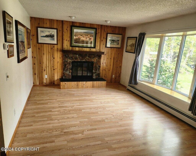 unfurnished living room featuring wood walls, light hardwood / wood-style floors, a stone fireplace, and a baseboard radiator