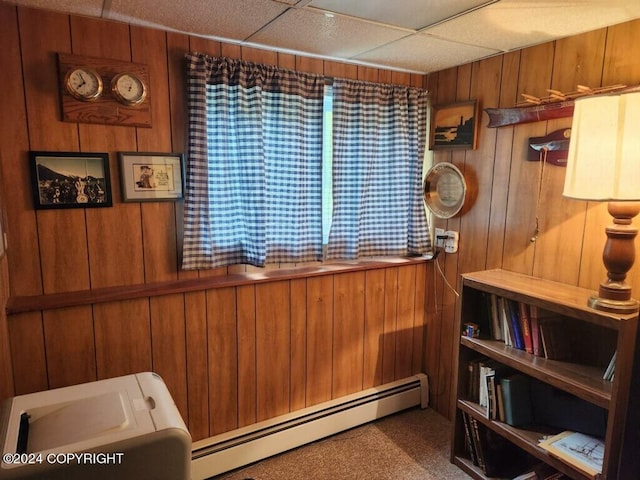 interior space with a drop ceiling, wooden walls, a baseboard heating unit, and carpet