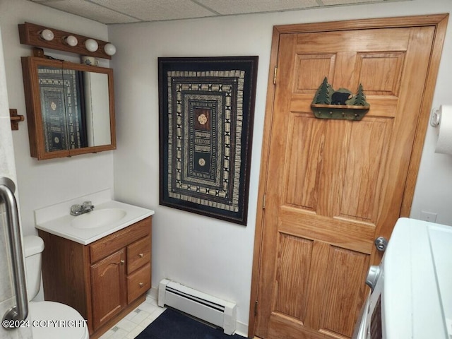 bathroom with vanity, tile patterned flooring, baseboard heating, a drop ceiling, and toilet