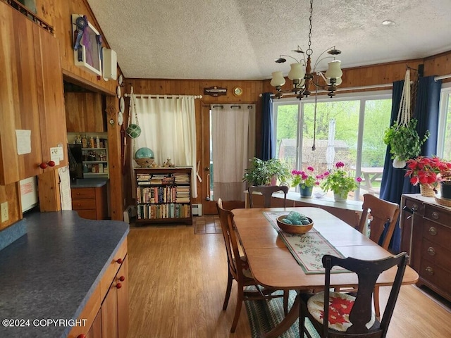 dining space with light hardwood / wood-style floors, a chandelier, wooden walls, and a textured ceiling