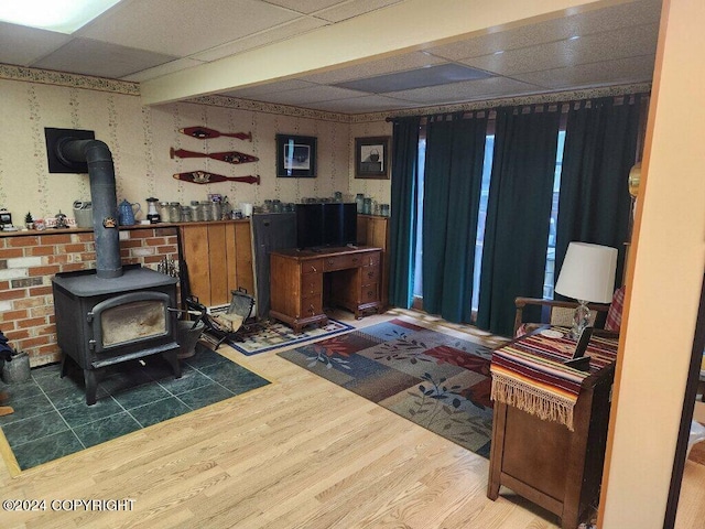 living area with a wood stove, a drop ceiling, and wood-type flooring