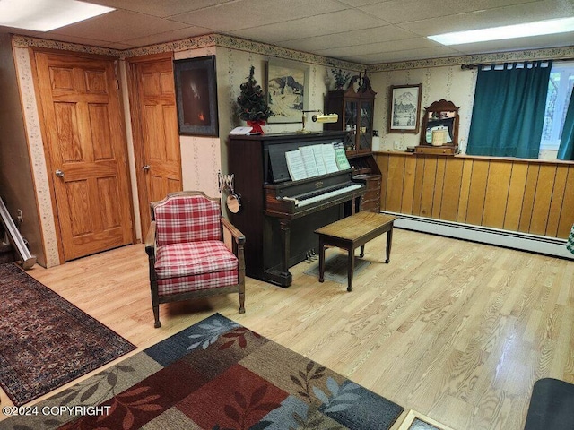 miscellaneous room featuring wood walls, light hardwood / wood-style flooring, baseboard heating, and a drop ceiling