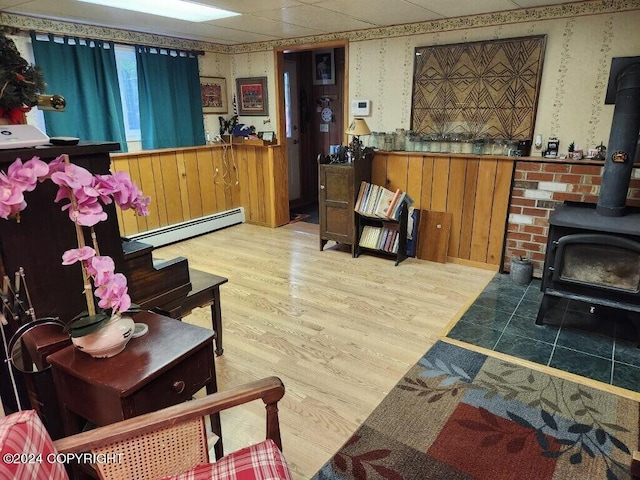 living room with a baseboard radiator, a drop ceiling, light wood-type flooring, and a wood stove