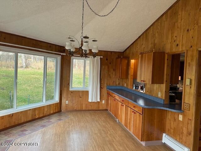 interior space with a textured ceiling, wooden walls, baseboard heating, a notable chandelier, and light wood-type flooring