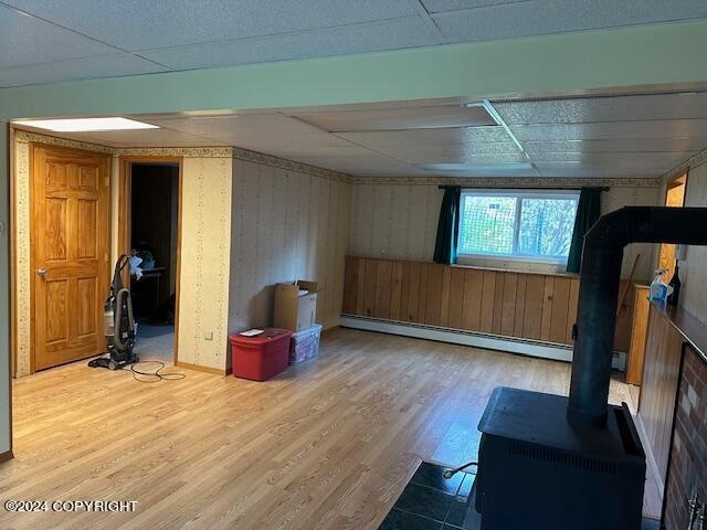 workout room featuring hardwood / wood-style flooring, baseboard heating, a drop ceiling, and a wood stove