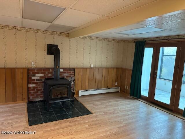 unfurnished living room with a paneled ceiling, hardwood / wood-style floors, a baseboard heating unit, and wooden walls