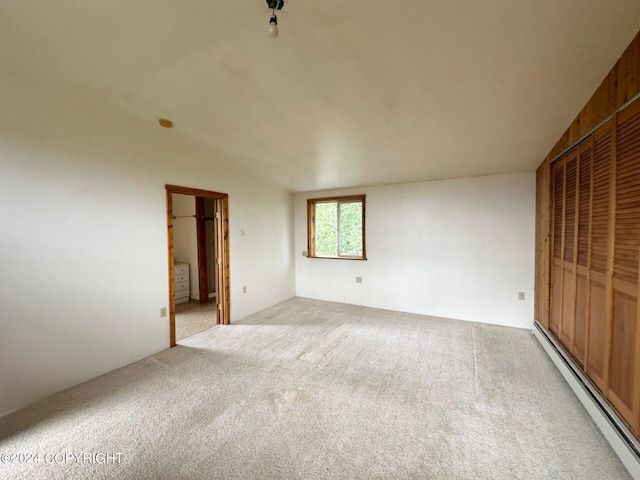 unfurnished bedroom featuring light colored carpet, a closet, and a baseboard heating unit