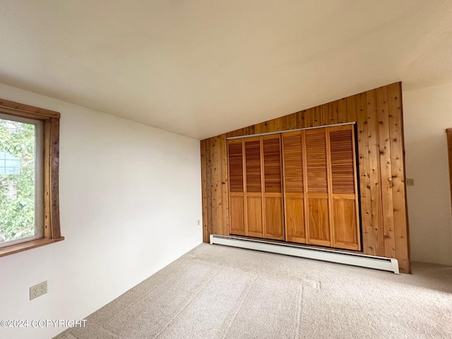 carpeted empty room with a baseboard radiator, vaulted ceiling, and wood walls