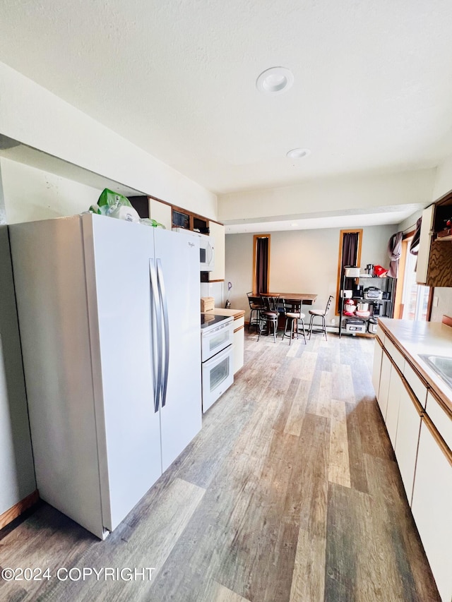 kitchen featuring white cabinetry, sink, white appliances, and light hardwood / wood-style flooring