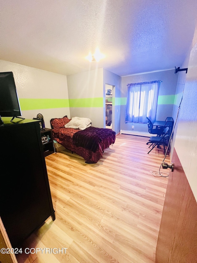 bedroom featuring light hardwood / wood-style flooring, a textured ceiling, and baseboard heating