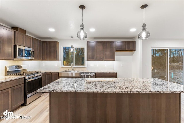 kitchen featuring pendant lighting, sink, stainless steel appliances, a center island, and dark brown cabinetry