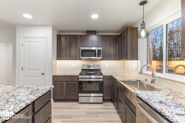 kitchen featuring sink, backsplash, hanging light fixtures, stainless steel appliances, and light hardwood / wood-style floors