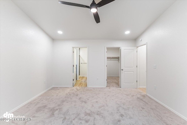 unfurnished bedroom with a spacious closet, light colored carpet, ceiling fan, and a closet