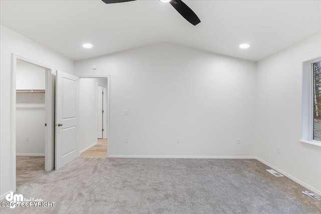 unfurnished bedroom with a spacious closet, vaulted ceiling, light carpet, a closet, and ceiling fan