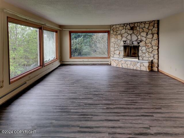 unfurnished living room with dark hardwood / wood-style flooring, a textured ceiling, a fireplace, and a baseboard radiator