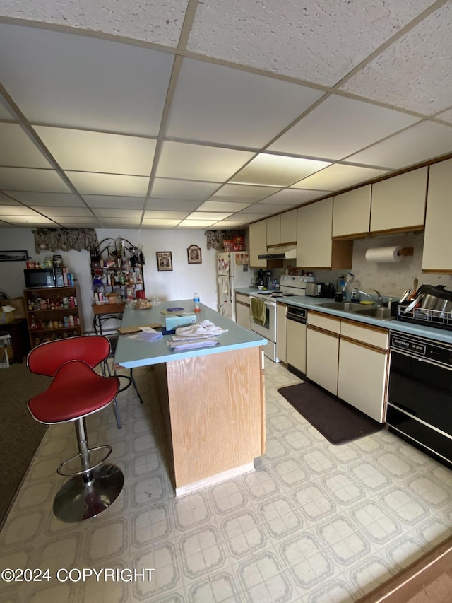 kitchen featuring sink, a center island, cream cabinets, a drop ceiling, and white appliances