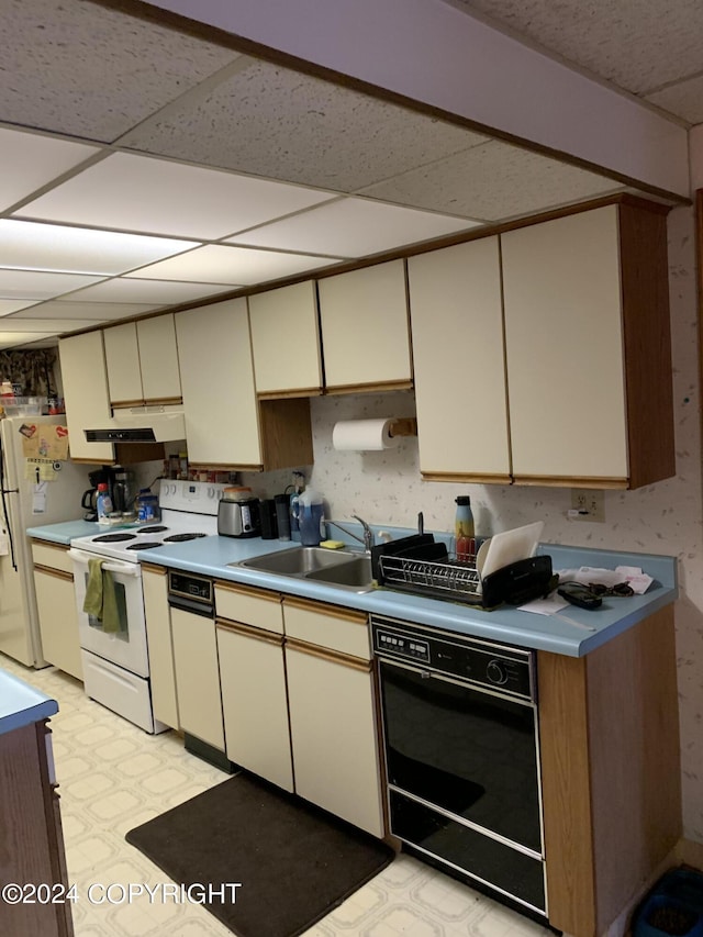 kitchen with sink, a paneled ceiling, white appliances, and cream cabinetry