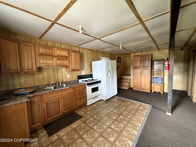 kitchen featuring wood walls, white appliances, dark countertops, light carpet, and a sink